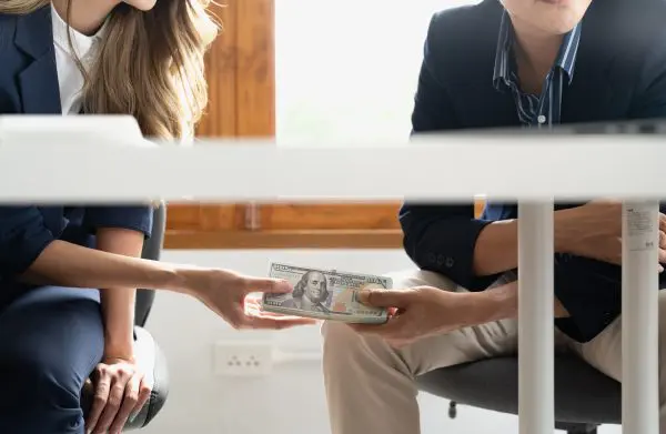 A businessman secretly passing money or bribe under a table to his partner. Business corruption concept. lavado-de-activos