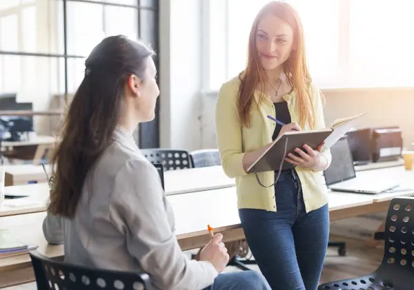 smiling-woman-holding-diary-pen-looking-her-colleague-office evaluacion-empleados